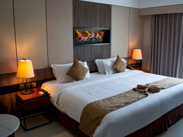 The image shows a hotel room with a large bed, bedside tables with lamps, and decorative art on the wall, creating a cozy ambiance.