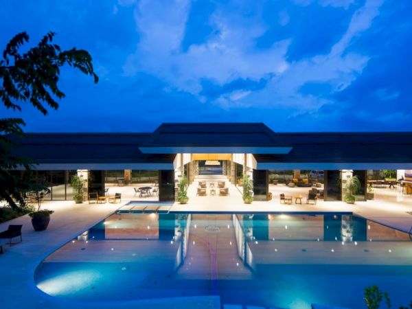 Modern building with a lit swimming pool in the foreground, set against a twilight sky.