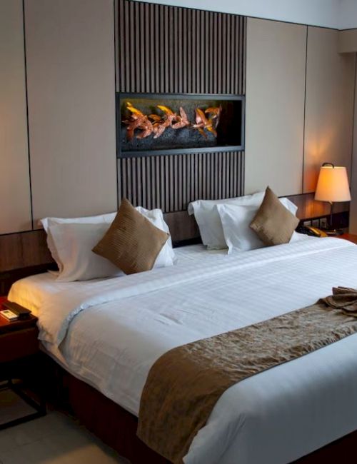 The image shows a cozy hotel room with a large bed, bedside tables with lamps, and a decorative painting on the wall above the bed.