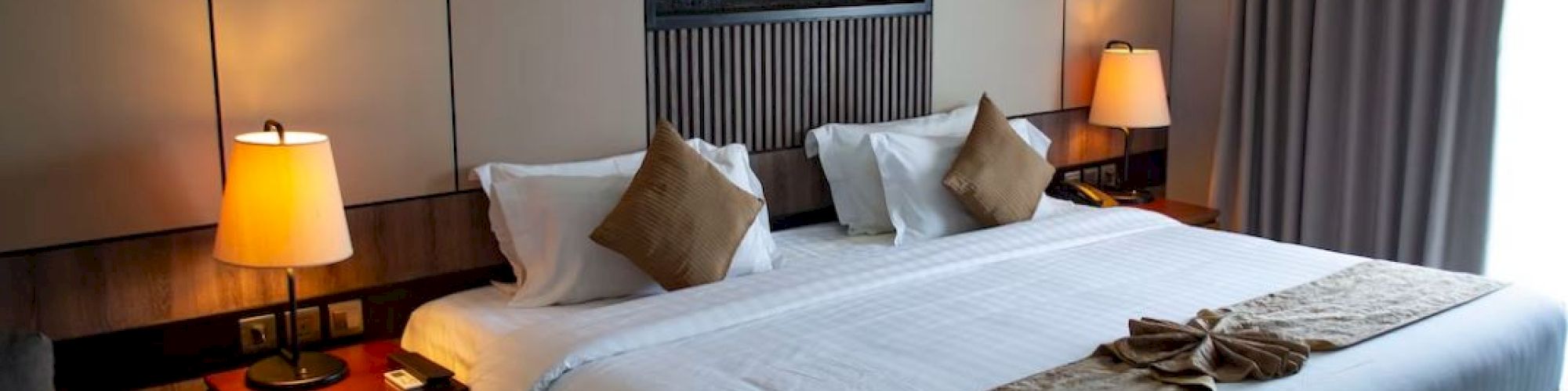 A neatly made hotel room with a large bed, decorative pillows, side tables with lamps, and a wall art piece above the bed.