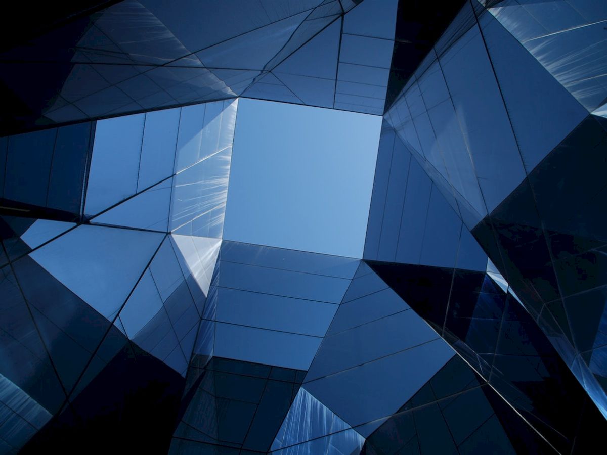Geometric glass structures form a pattern, reflecting the sky. It creates a modern, abstract architectural view with a central opening.