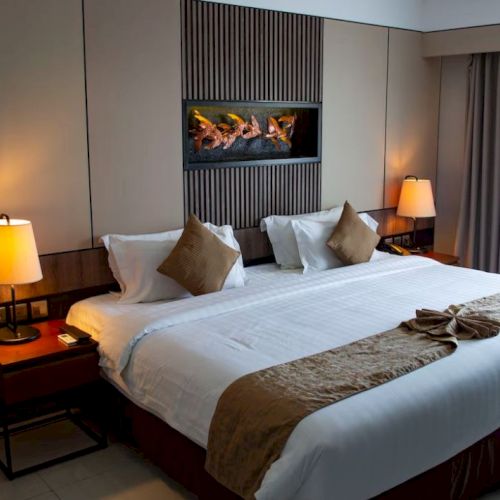 A neatly arranged hotel room with a large bed, pillows, bedside tables, lamps, and a decorative wall feature above the bed.