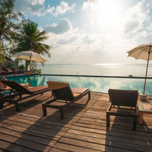 A serene poolside view with deck chairs, umbrellas, and a tranquil sea under a bright sky.