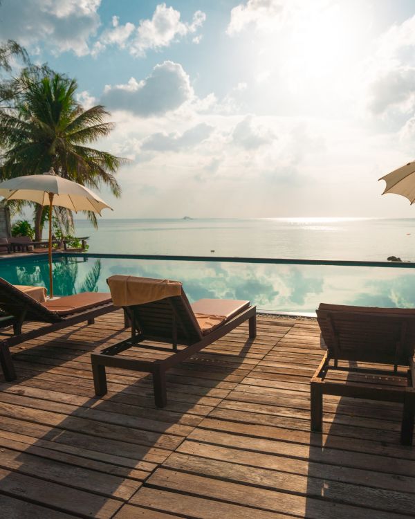 A serene poolside view with deck chairs, umbrellas, and a tranquil sea under a bright sky.