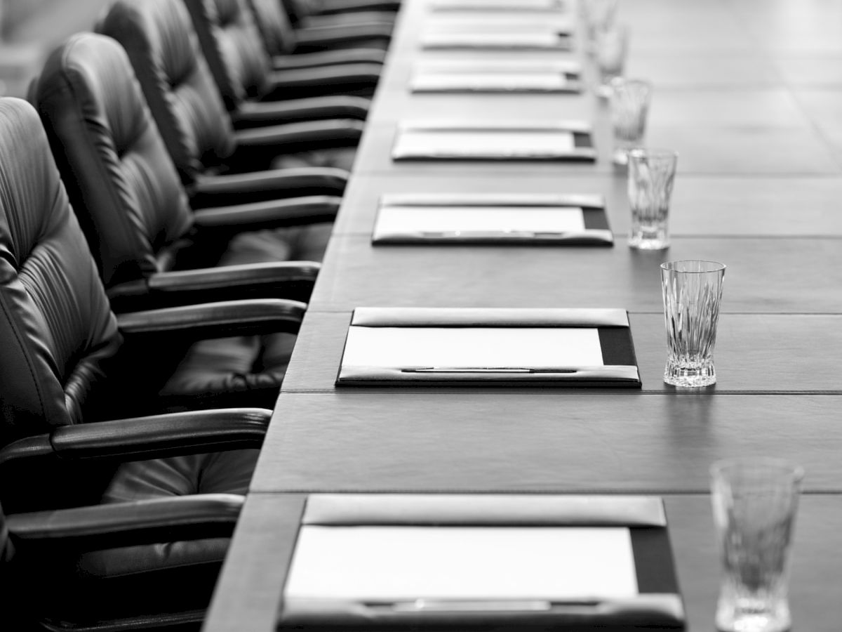 A boardroom table with leather chairs, each spot set with a notepad, pen, and glass, prepared for a meeting or conference.
