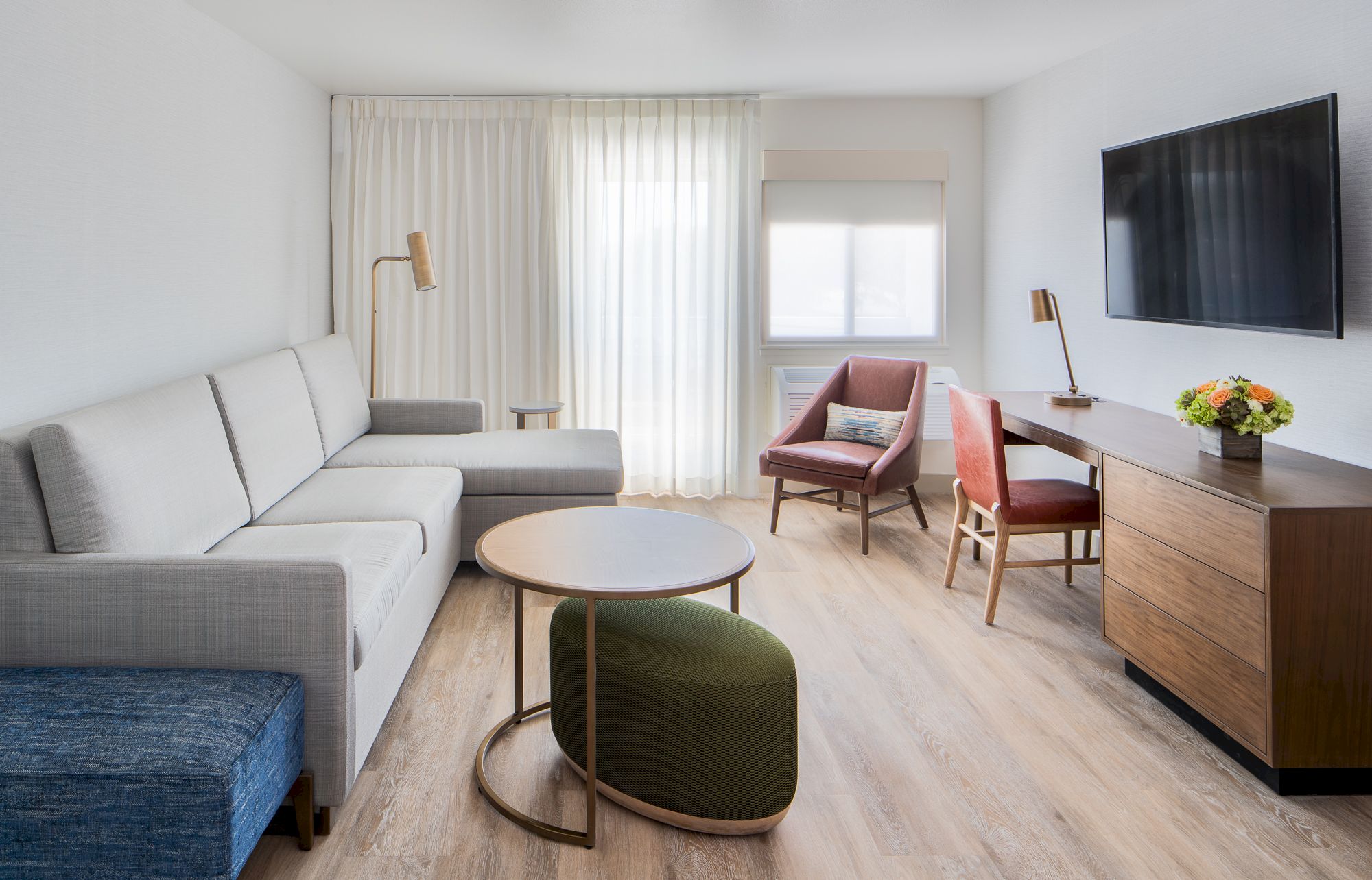 A modern living room with a sectional sofa, chairs, coffee table, TV, and a wooden dresser, under soft natural light from a window.