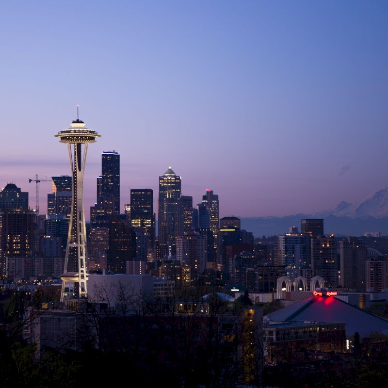 The image shows a city skyline at dusk, including a lit tower and distant mountains, under a clear sky with a gentle gradient of colors.