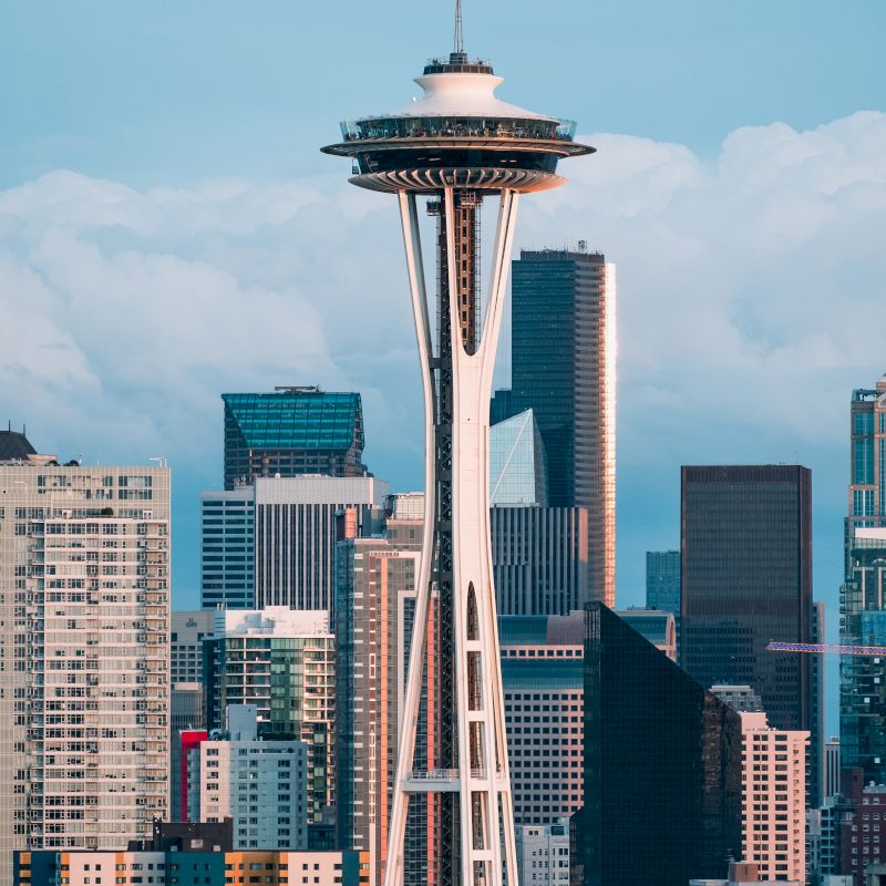 The image shows the Space Needle in Seattle, surrounded by various skyscrapers, under a partly cloudy sky.