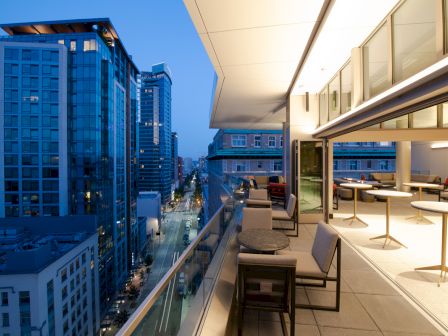 A rooftop terrace with seating overlooks a cityscape with modern tall buildings during twilight.