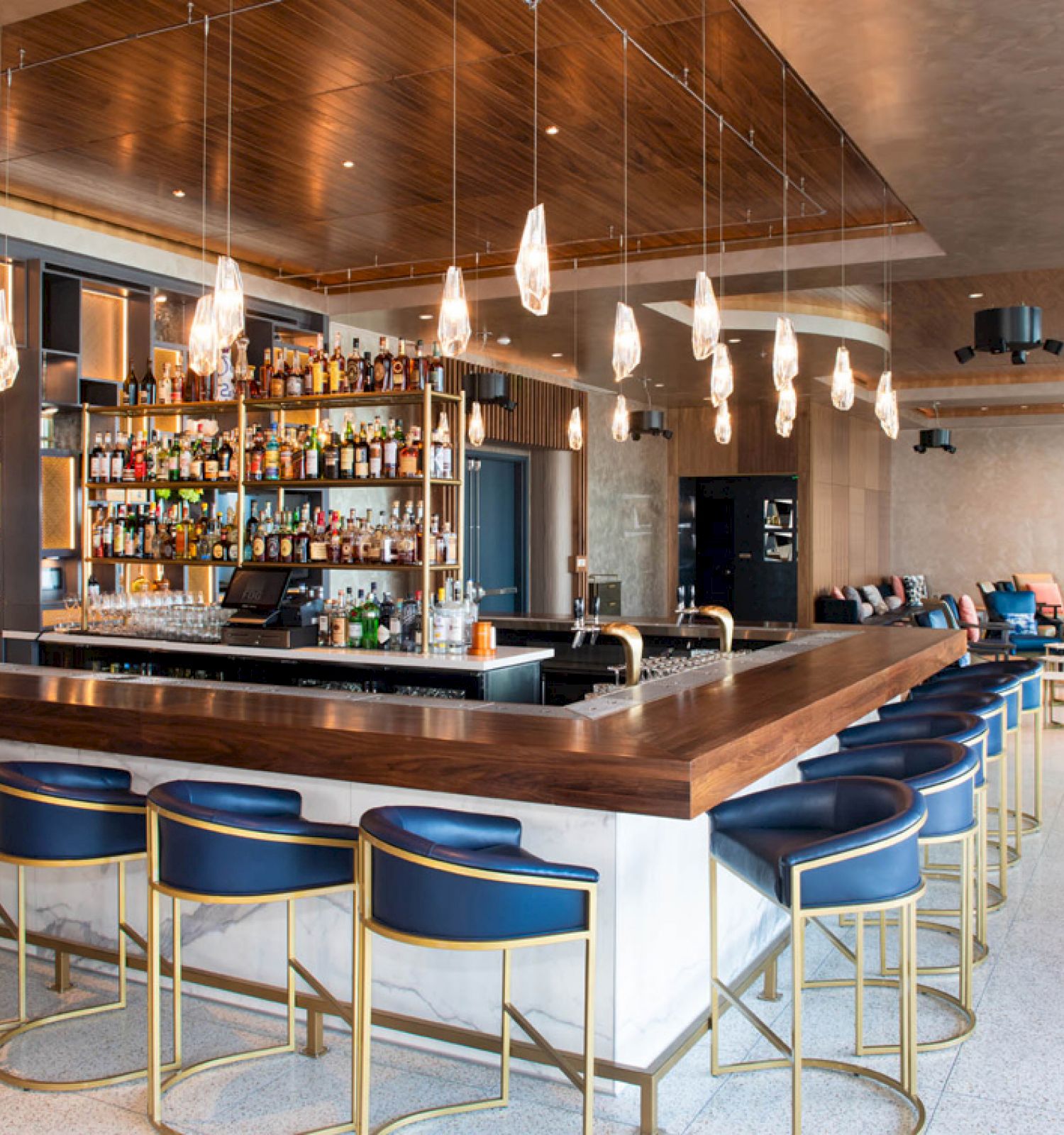 A modern bar with a central counter, high stools, hanging lights, and a well-stocked back display.