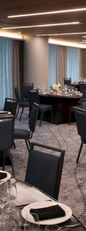 The image shows an elegantly set dining area with round tables, chairs, and soft lighting, suitable for a formal event or gathering.