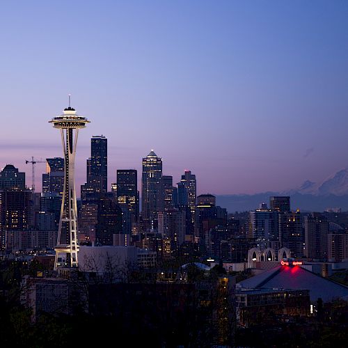 Seattle skyline at dusk with the iconic Space Needle, buildings, and Mount Rainier in the background against a purple sky.
