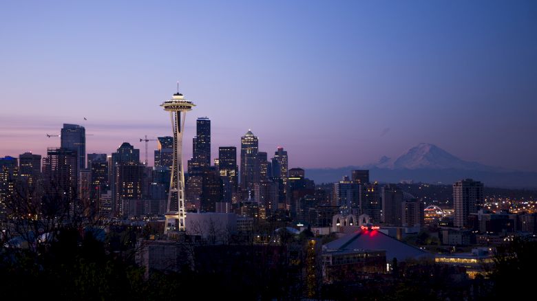 Skyline of Seattle with the Space Needle prominently featured, set against a twilight sky and with a mountain in the distance.