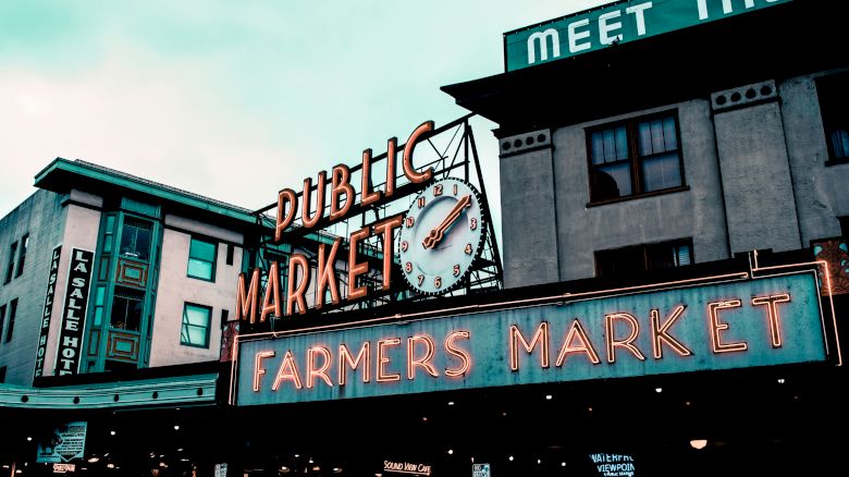 The image shows a public market entrance with neon signs for "Public Market" and "Farmers Market," featuring a prominent clock above.